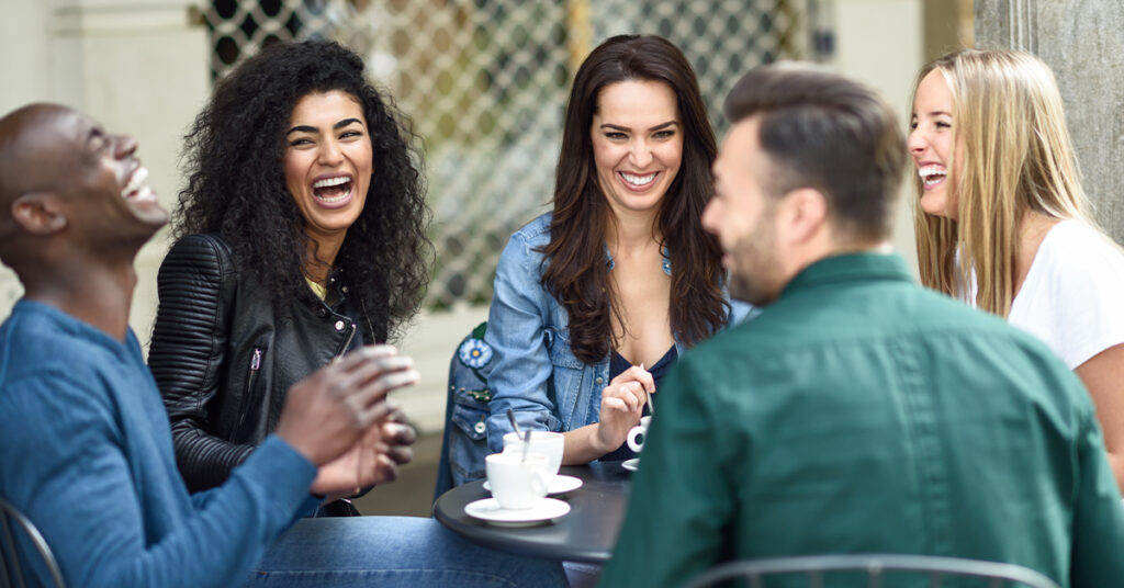Grupo de pessoas conversando em uma cafeteria, ilustrando como a audição e socialização são fundamentais para momentos de convivência e troca entre amigos.